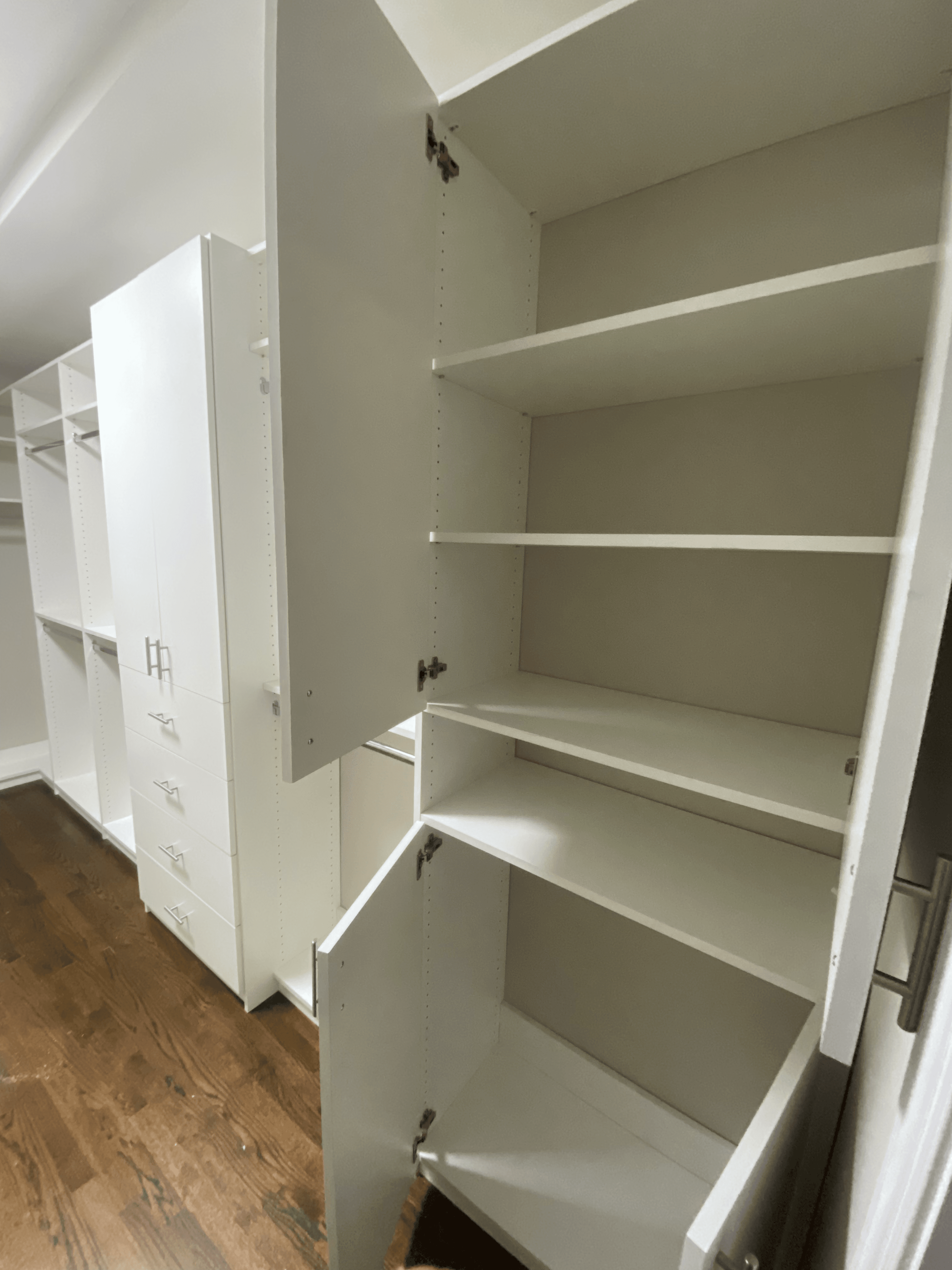 White custom walk-in closet system with open shelves, drawers, and cabinet doors over hardwood floors.
