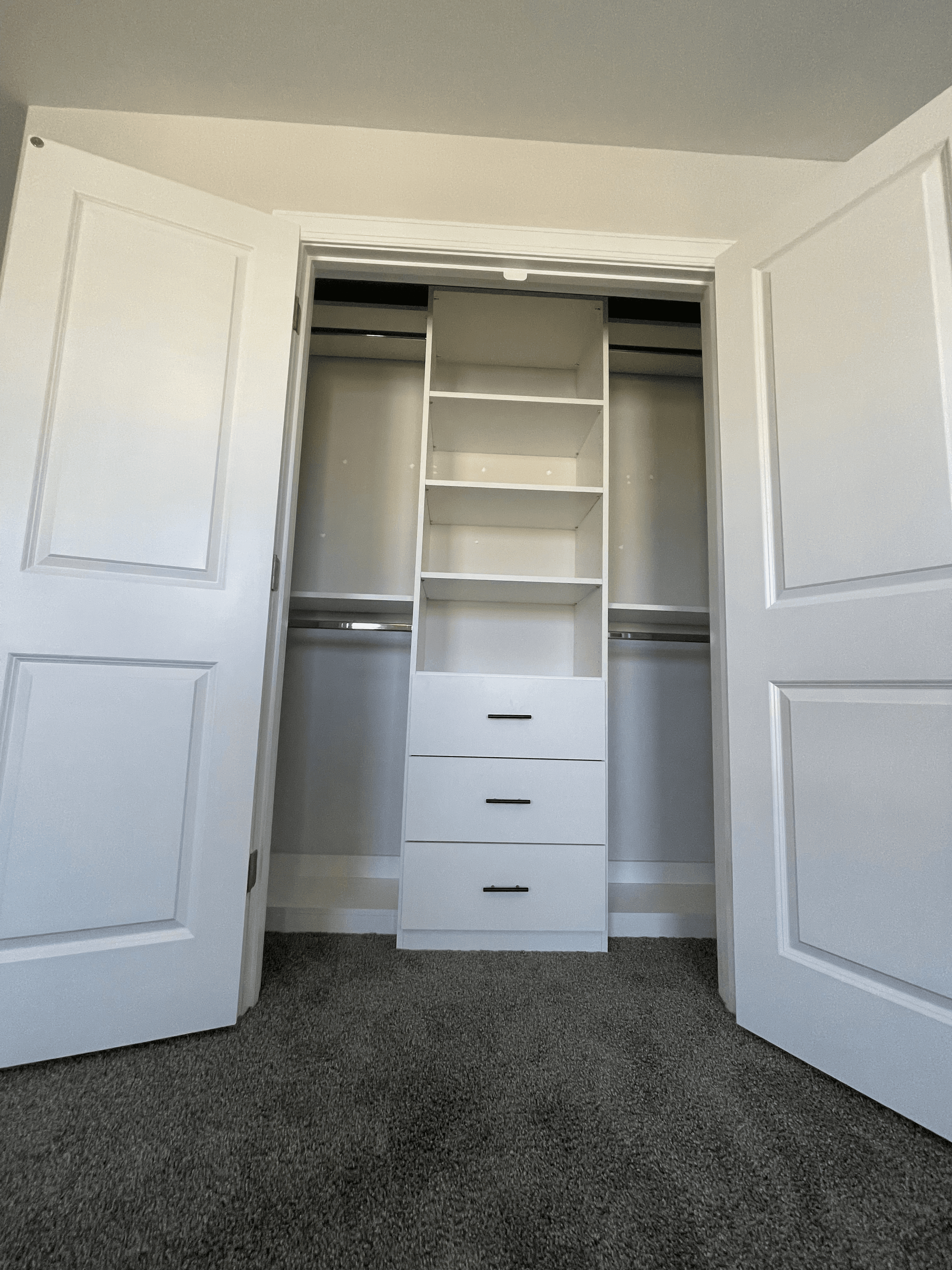 Open white closet doors revealing a built-in organizer with shelves, drawers, and hanging rods.