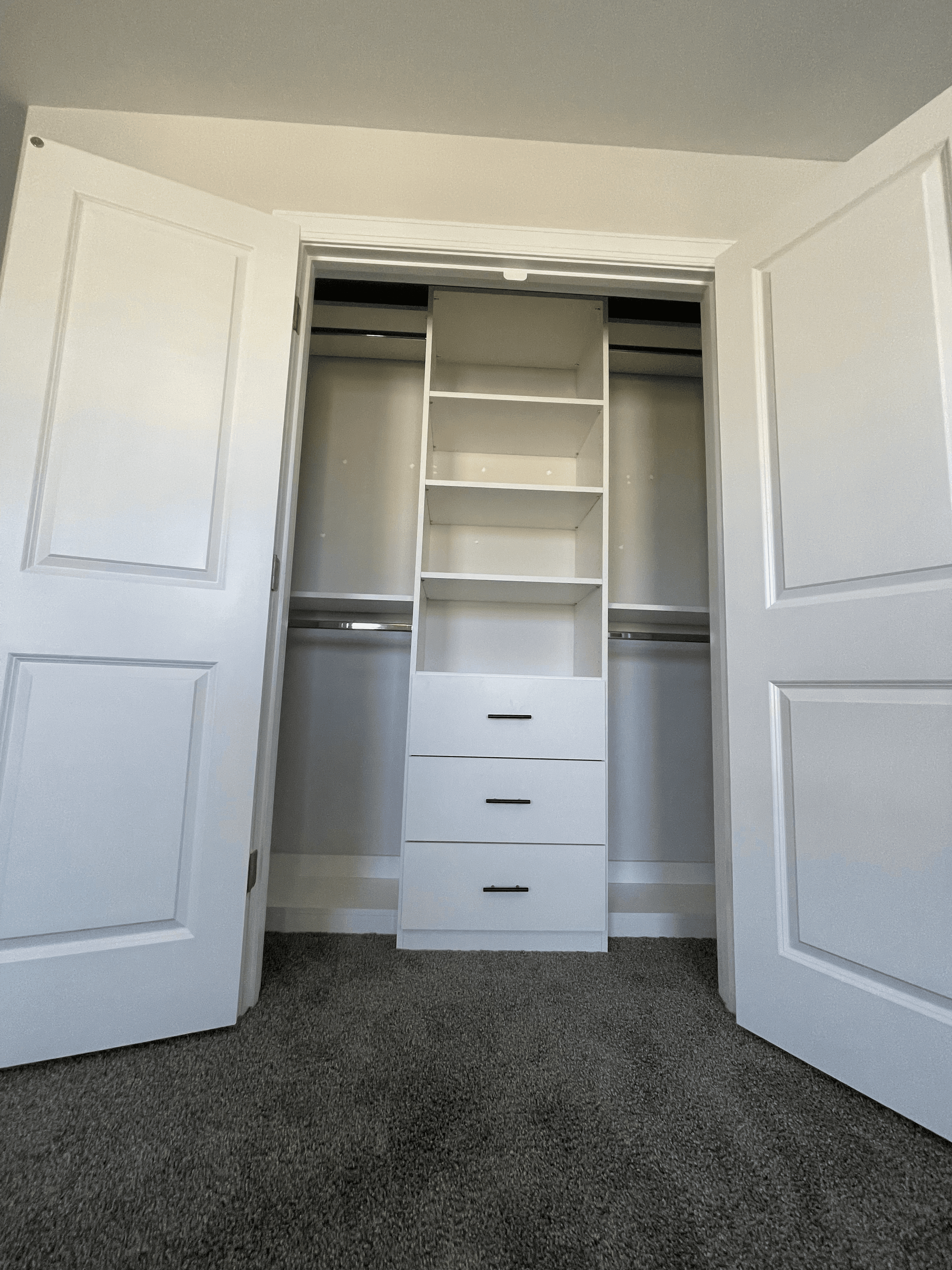 Open white closet featuring built-in central shelving, three drawers, and dual hanging rods.