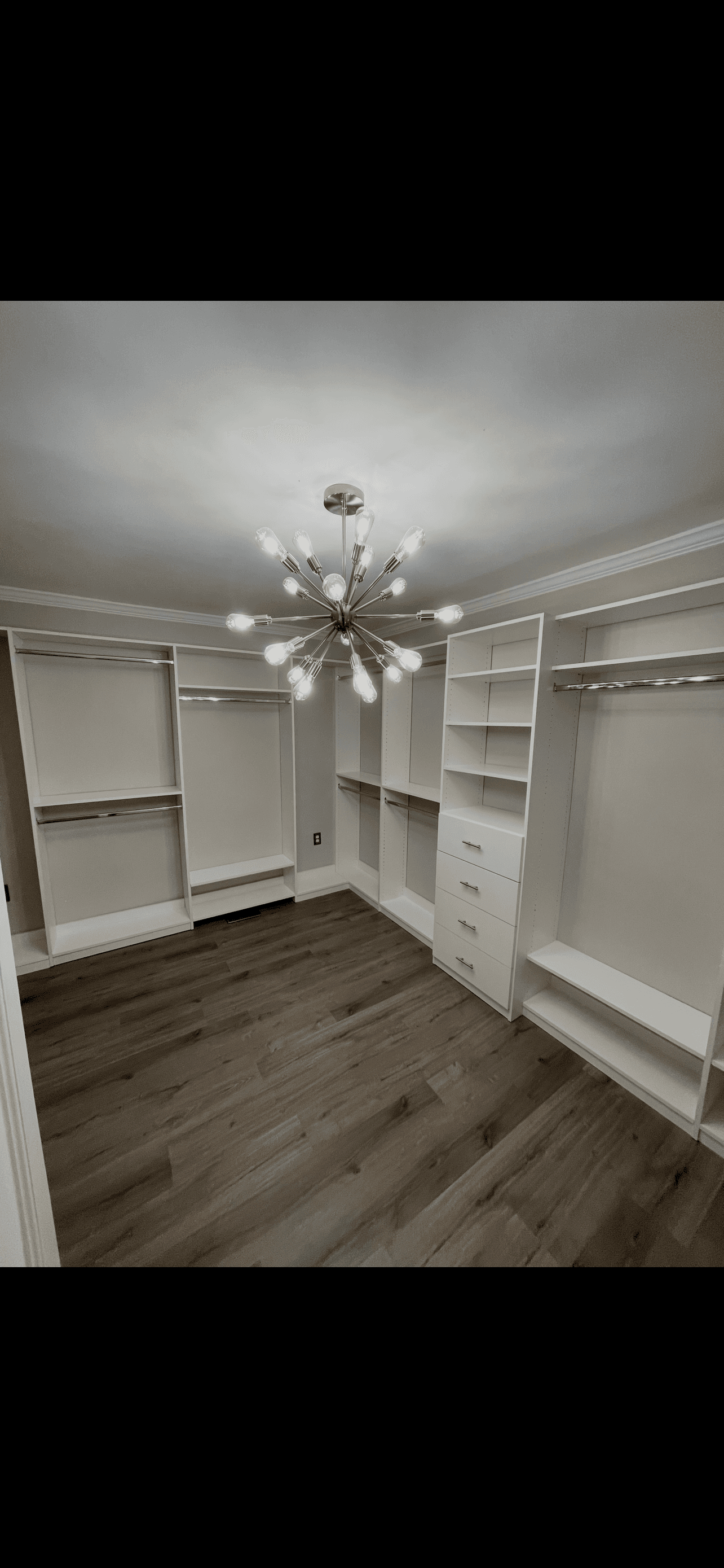 Empty walk-in closet with white custom shelving, dark wood floors, and a modern sputnik chandelier.