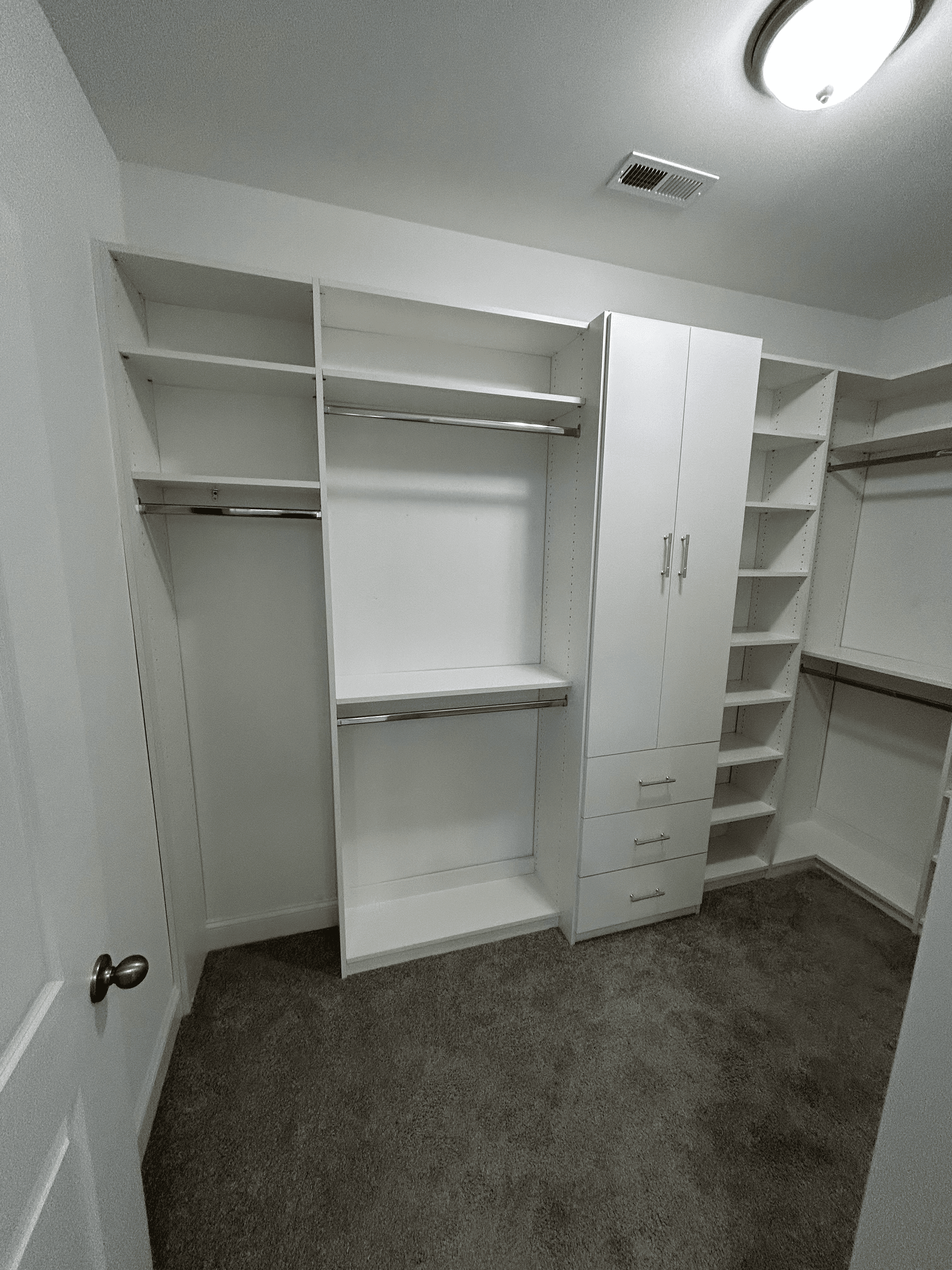 White walk-in closet featuring custom shelving, hanging rods, and a cabinet with gold hardware.