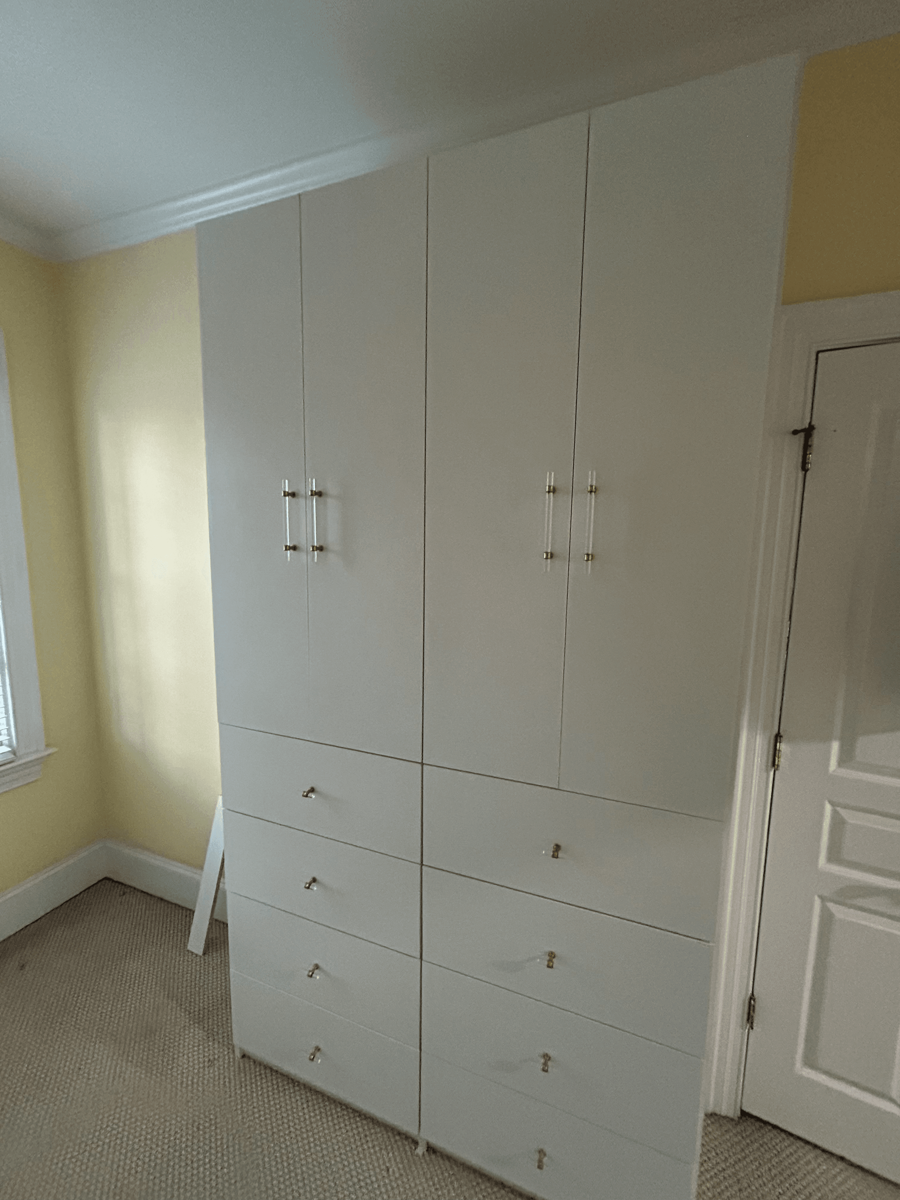 Floor-to-ceiling white built-in closet with gold and acrylic hardware against a yellow wall.