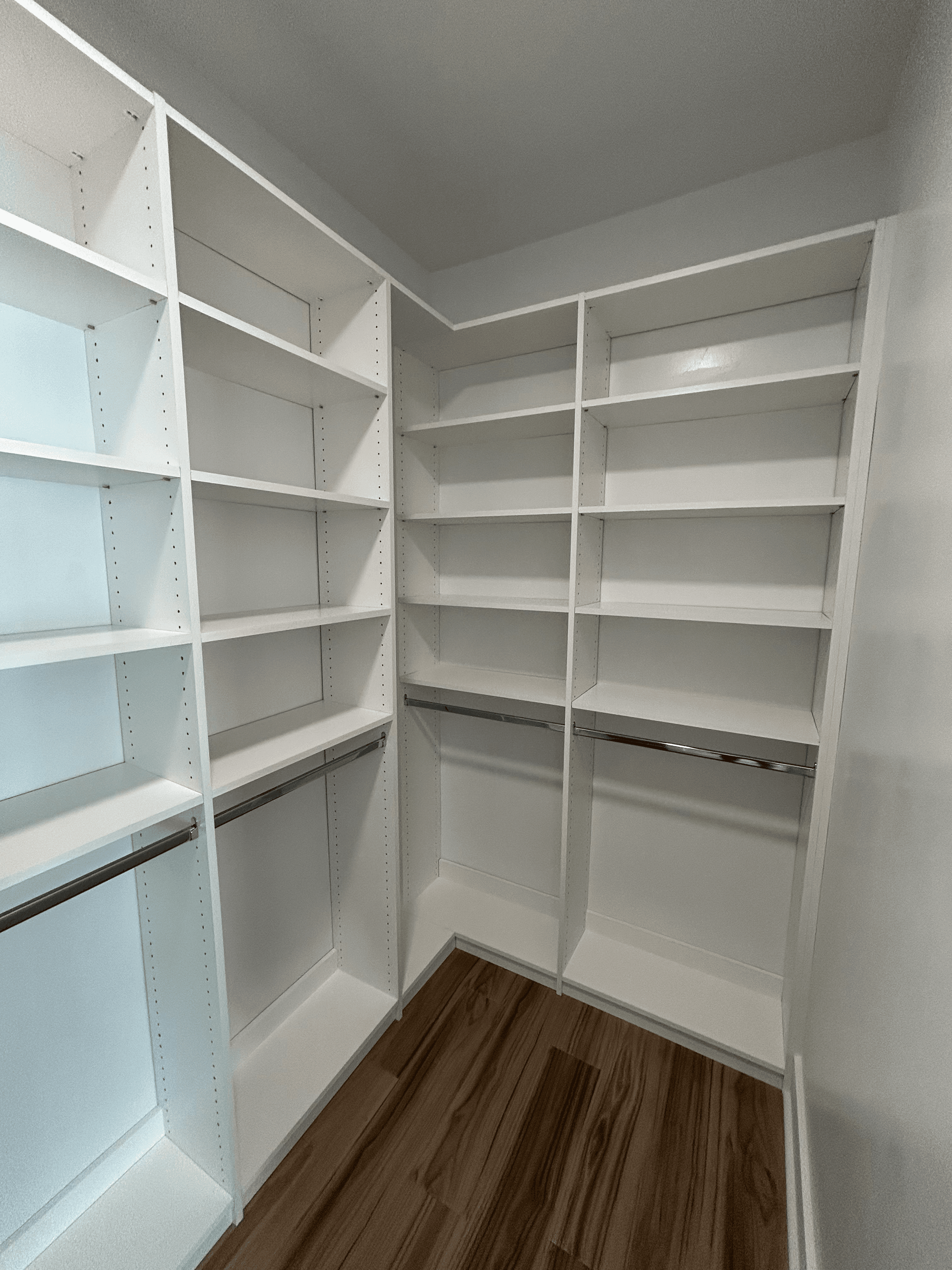 Empty white walk-in closet featuring built-in shelving, metal hanging rods, and dark wood flooring.