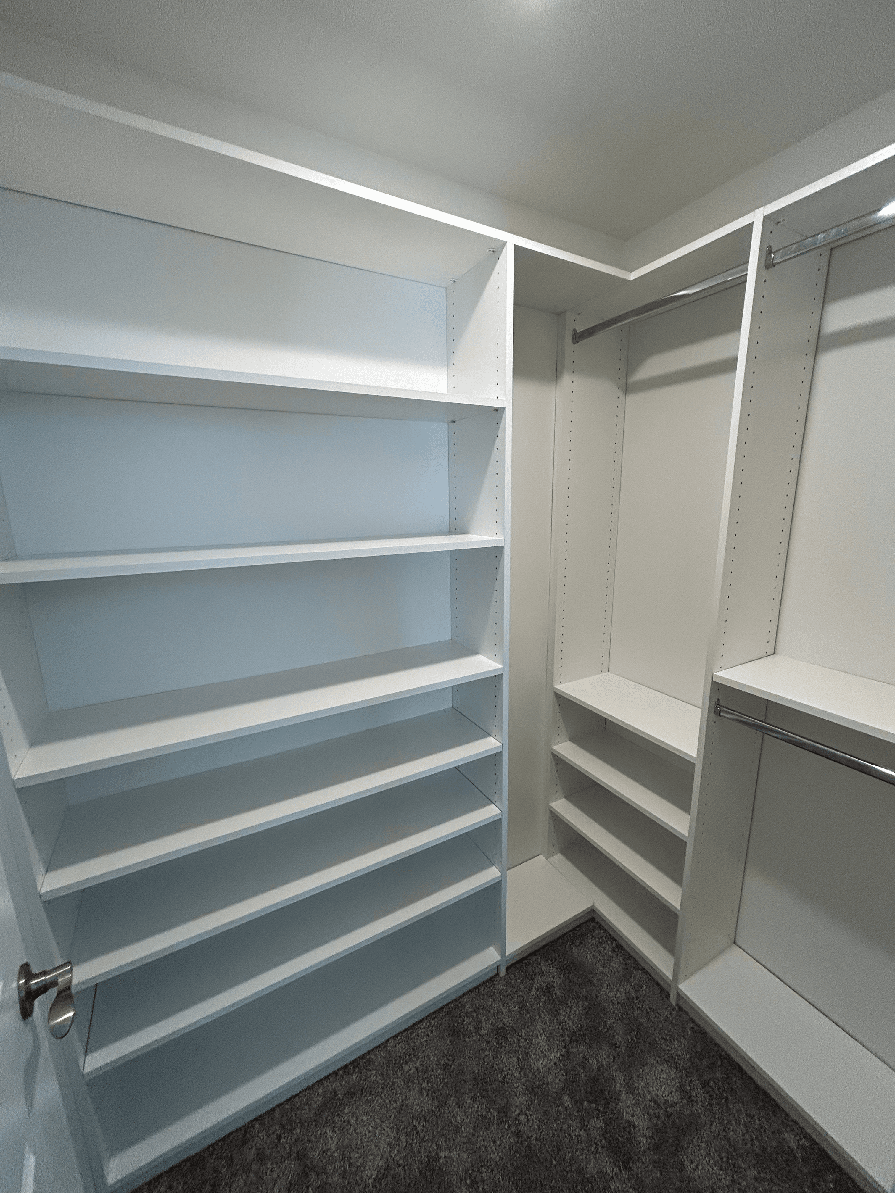 Empty white built-in walk-in closet system with multiple shelves and metal hanging rods.