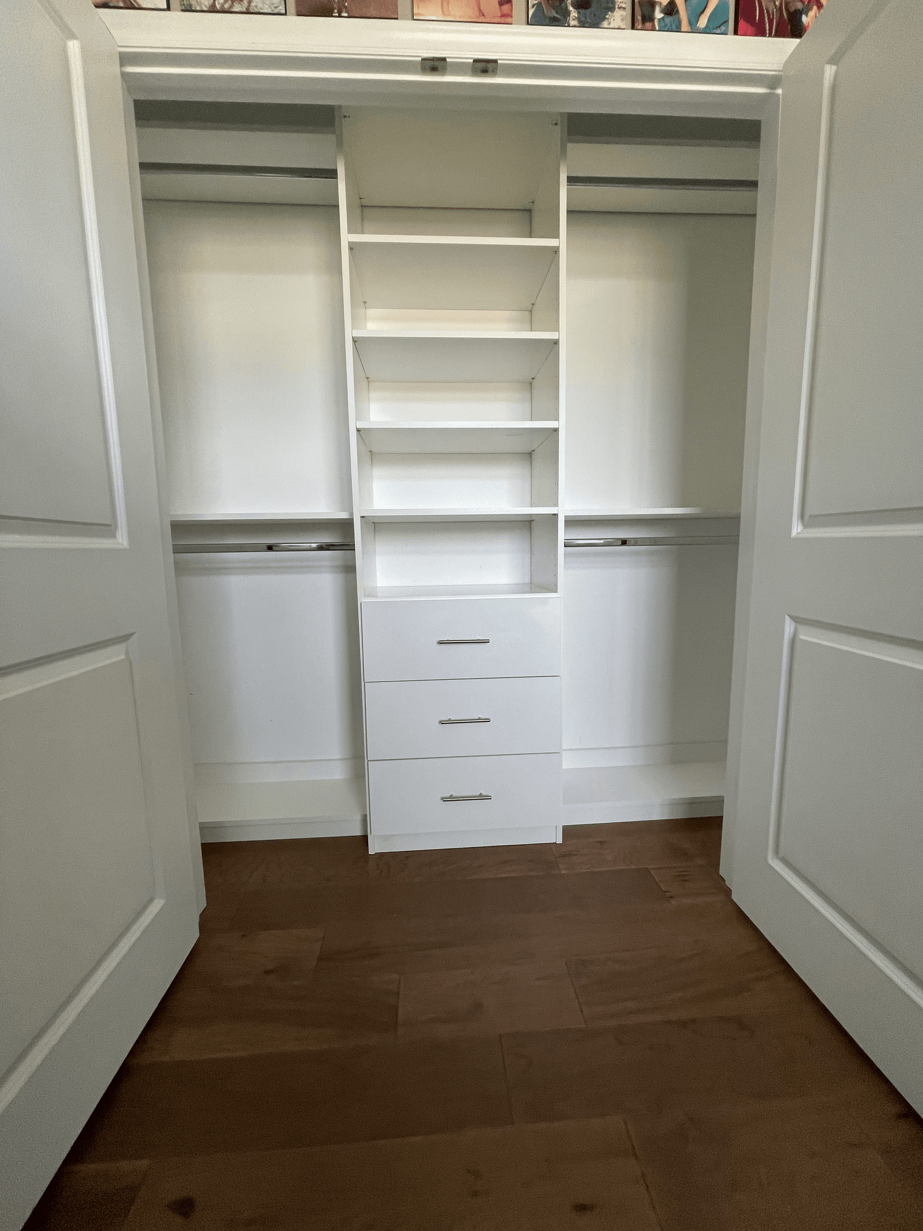Empty white closet organizer with shelves and drawers between two open white paneled doors.