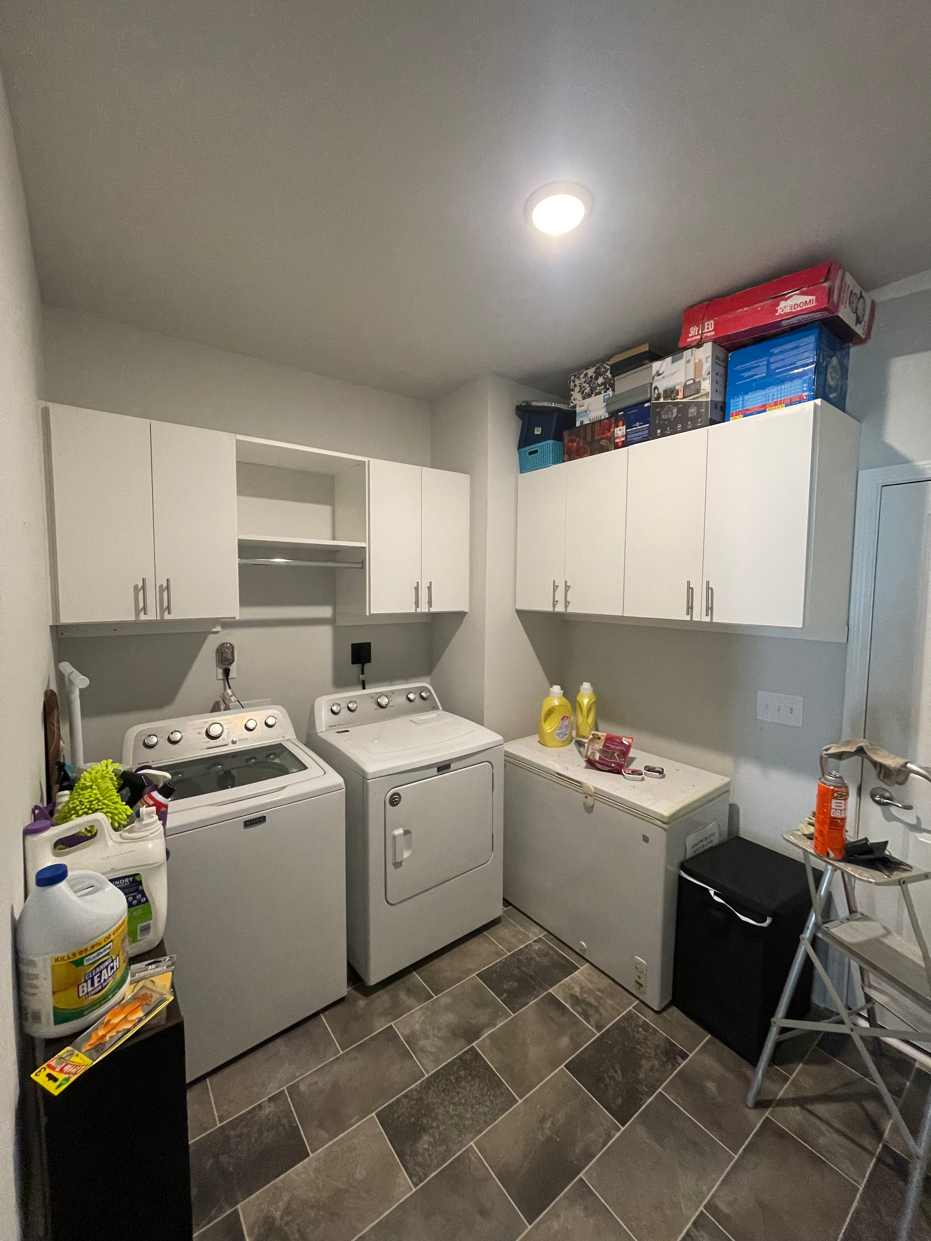 Laundry room with white washer and dryer, overhead cabinets, chest freezer, and grey tiled floor.